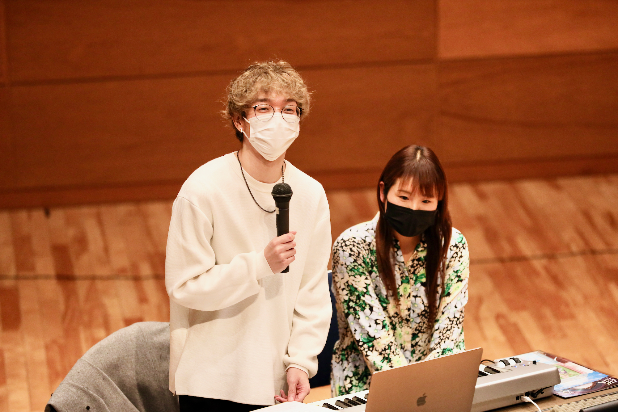 映像音楽のレコーディング現場についてお話している助手の安井さんと富貴先生の写真